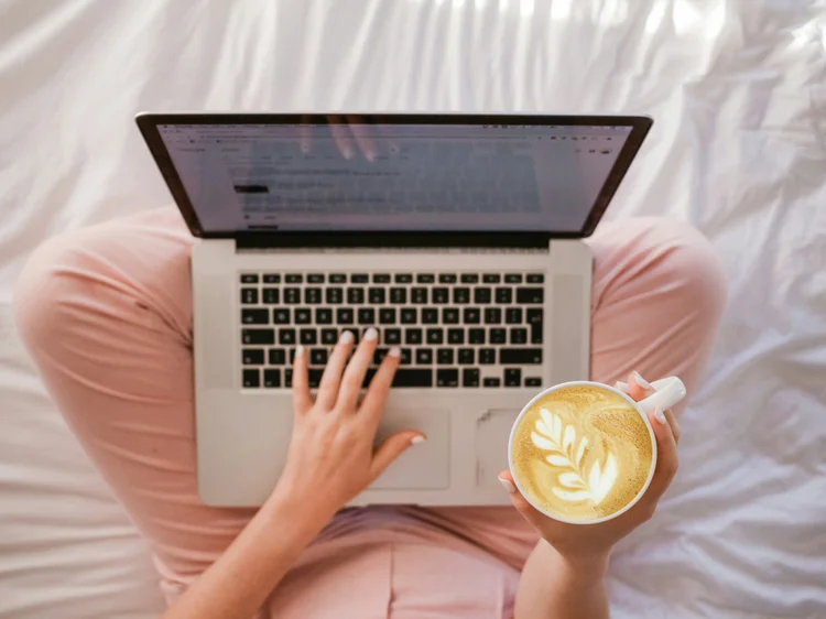 Person on a bed using a laptop with coffee
