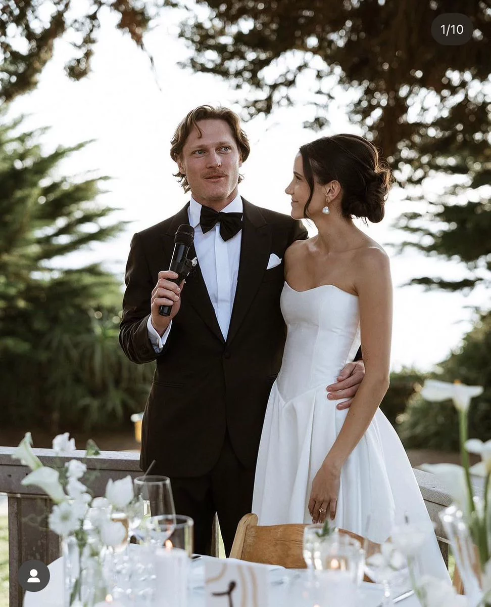 Groom giving speech with bride looking on lovingly at wedding reception
