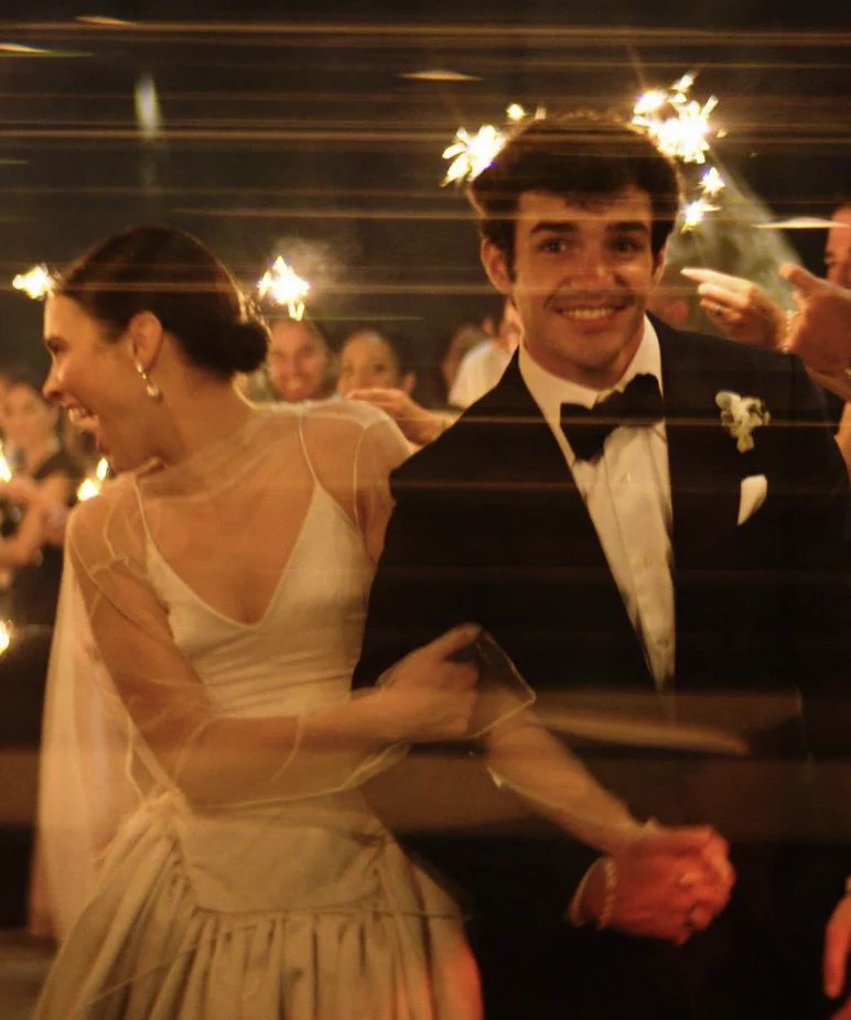 Groom smiling with bride surrounded by sparklers at wedding